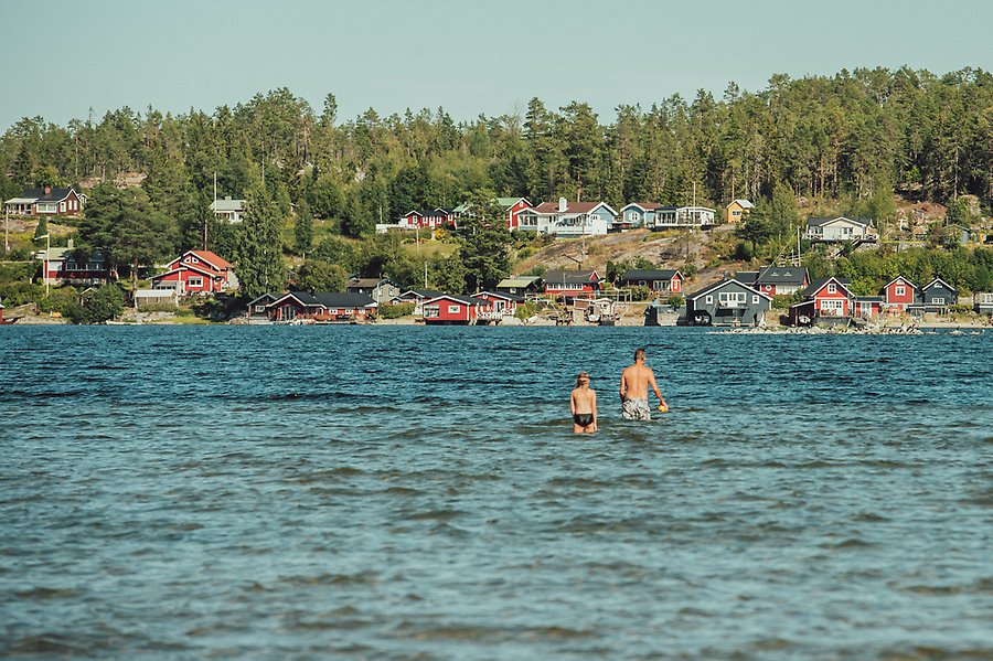 Två personer badar i havet, i bakgrunden syns flera hus.