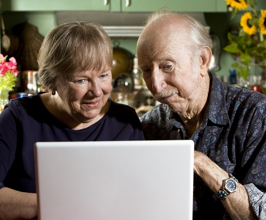Äldre kvinna och man sitter framför en laptop och pratar om någonting de ser på skärmen.