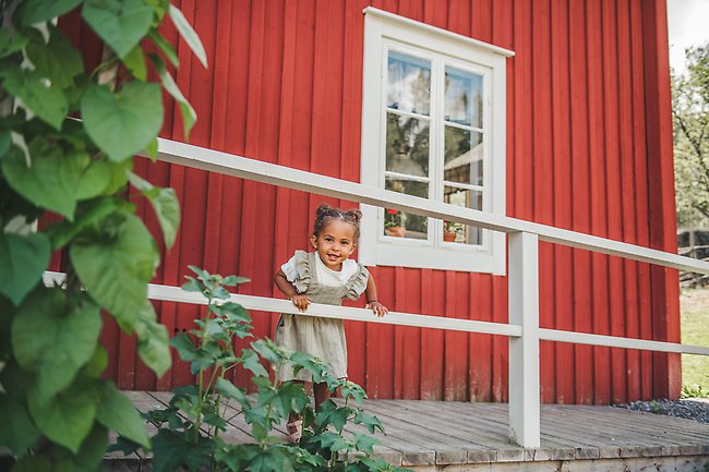 Ett barn står på en bro vid ett rött hus och tittar ut över en stor gård.