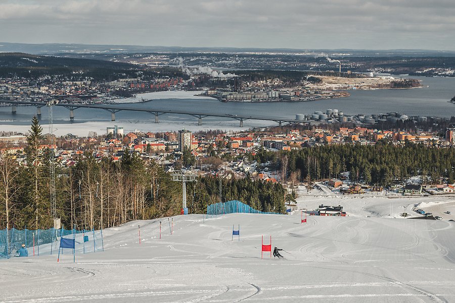 En slalombacke i stadskärnan. En person åker slalom mellan röda och blå portar med utsikt över Sundsvalls stenstad, havet och Alnön.