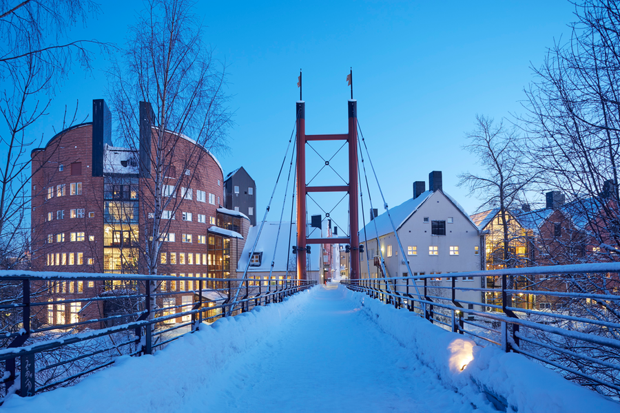 Vinterbild över en bro som leder till två stora byggnader.