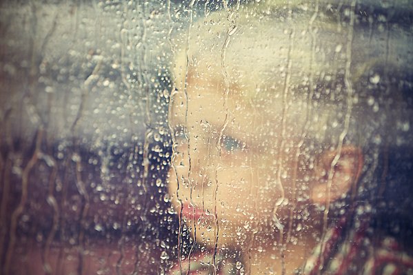 Barn tittar ut genom fönster, det regnar.